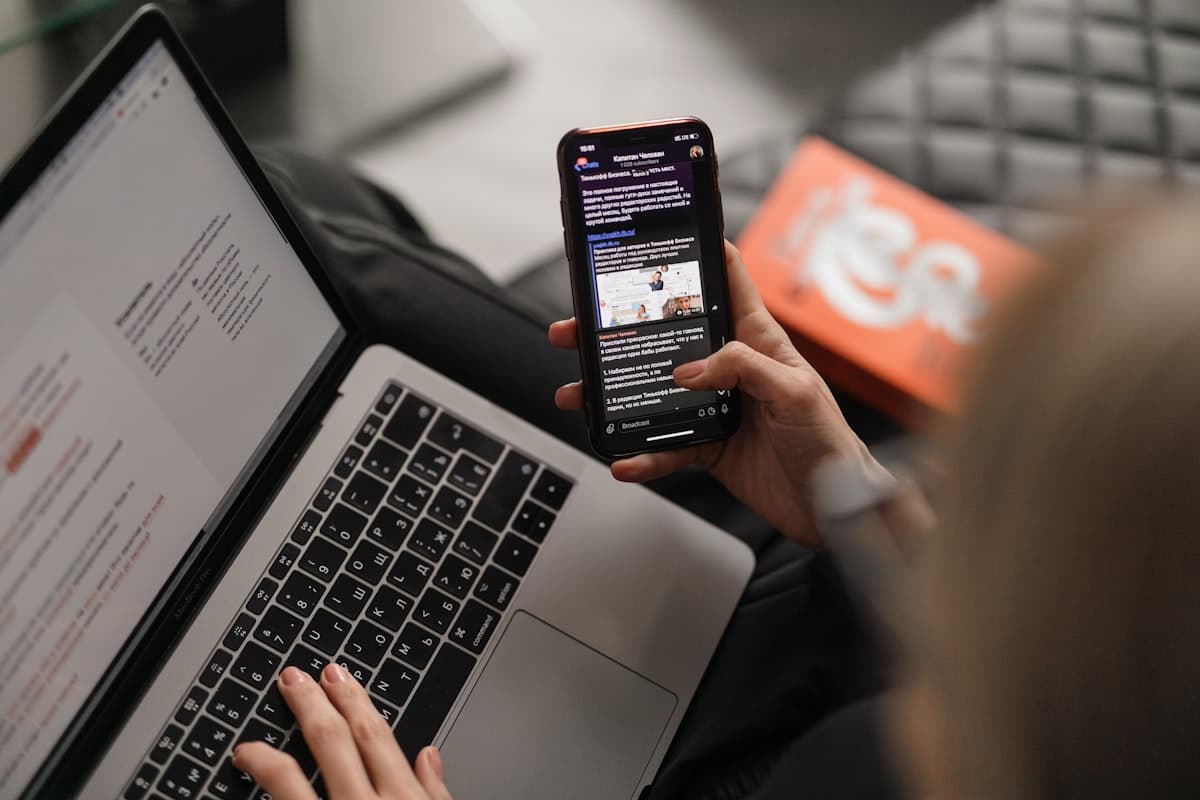 Personne consultant son téléphone, un ordinateur portable ouvert devant elle